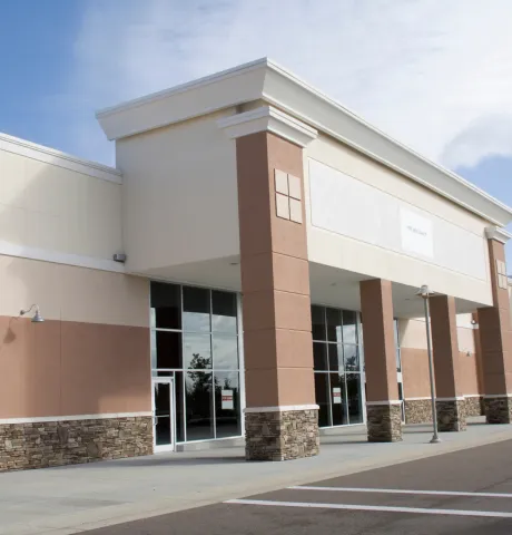 Commercial building construction in Los Angeles showing a modern retail storefront exterior with glass entry doors, stucco facade, stone accents, columns, and parking area
