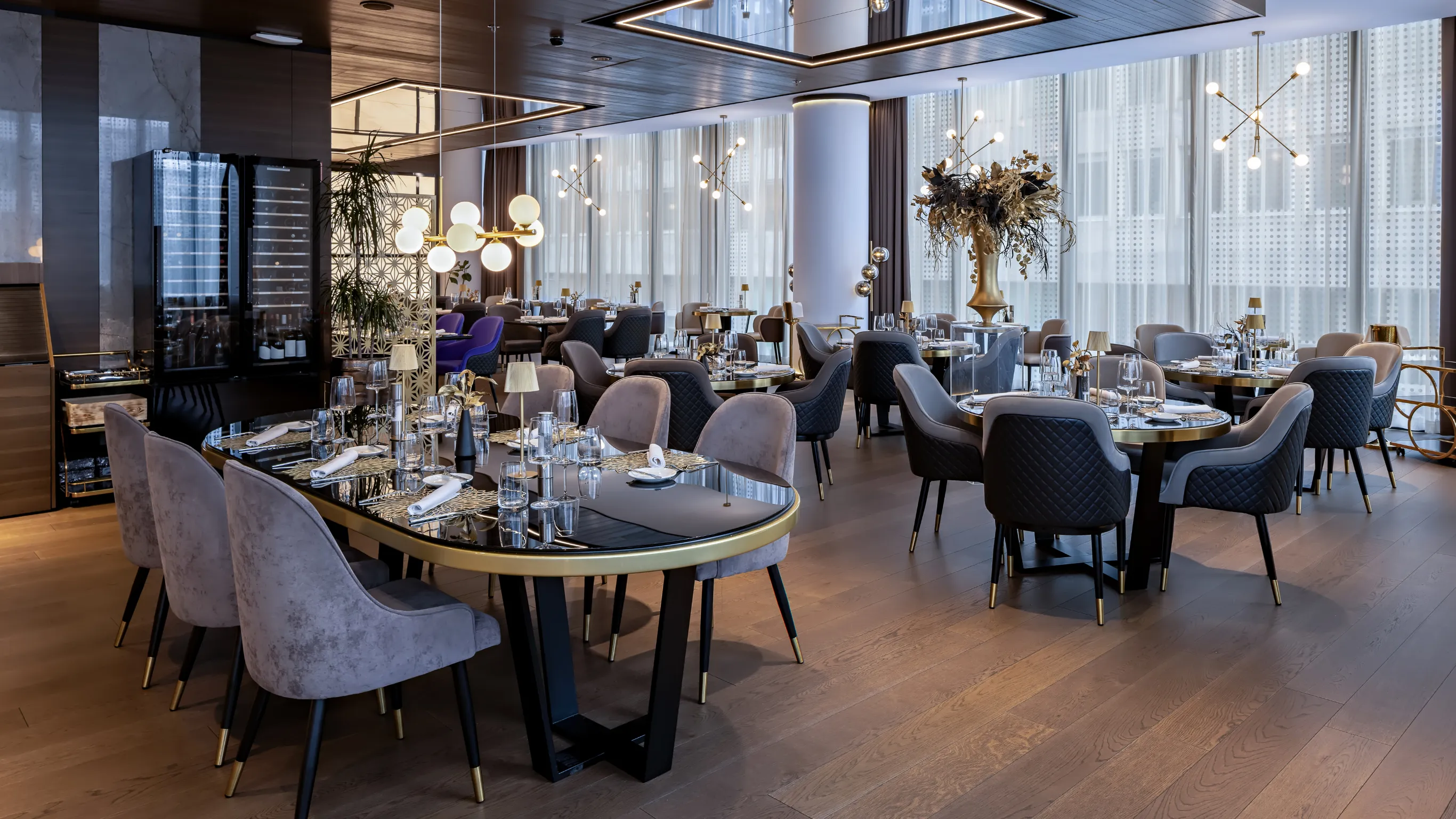 After commercial remodeling project in Los Angeles showing a luxury restaurant interior with elegant dining tables, upholstered chairs, modern lighting, wood flooring, wine display, and upscale finishes