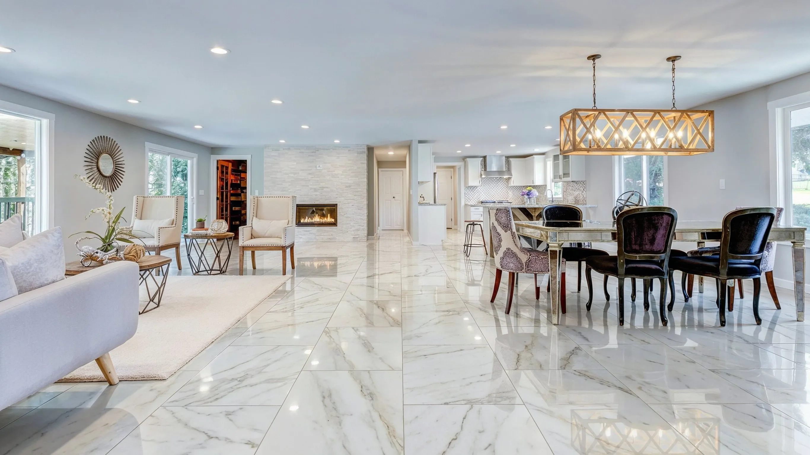 After flooring installation project in Los Angeles showing a bright open living and dining area with polished white tile flooring, modern kitchen, fireplace, recessed lighting, and elegant interior finishes