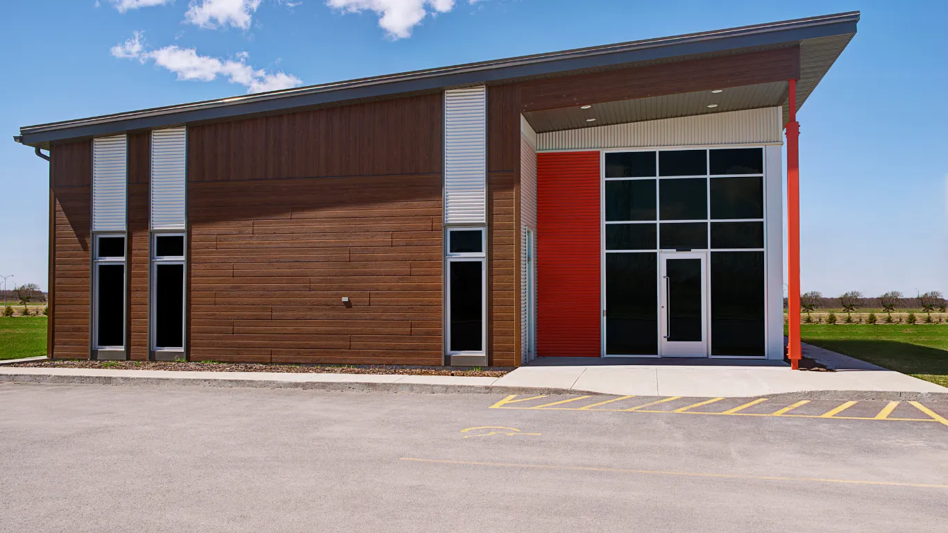 Commercial building construction project in Los Angeles showing a modern business building exterior with wood siding, red accent wall, large glass entrance, parking area, and clean contemporary design