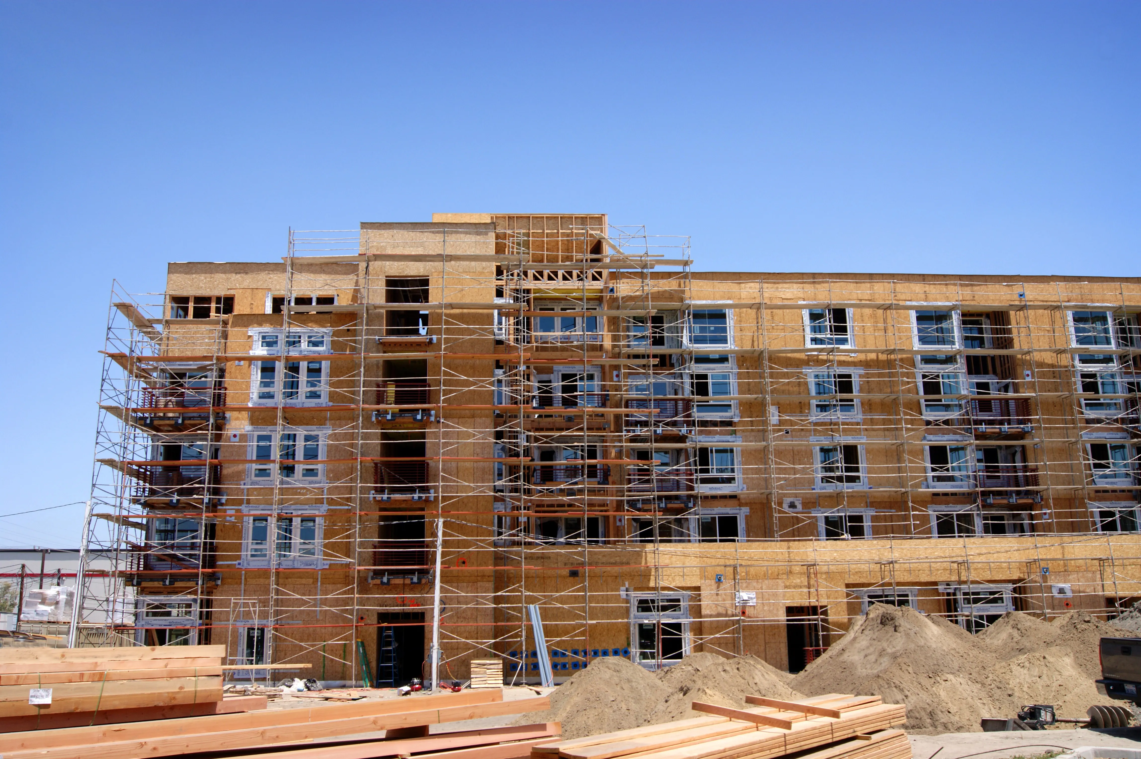 Los Angeles commercial building construction project with multistory framing, exterior sheathing, scaffolding, installed windows, balconies, and building materials on site