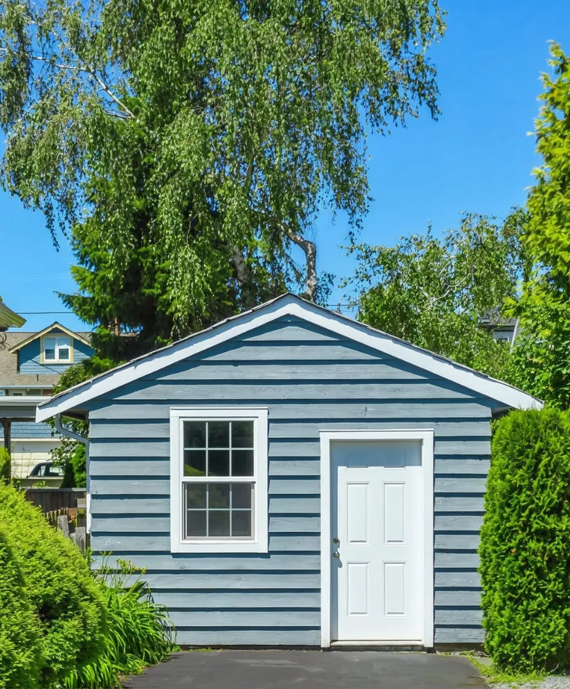 Los Angeles garage conversion ADU project showing a detached backyard structure with blue siding, white entry door, window, driveway access, and private landscaping