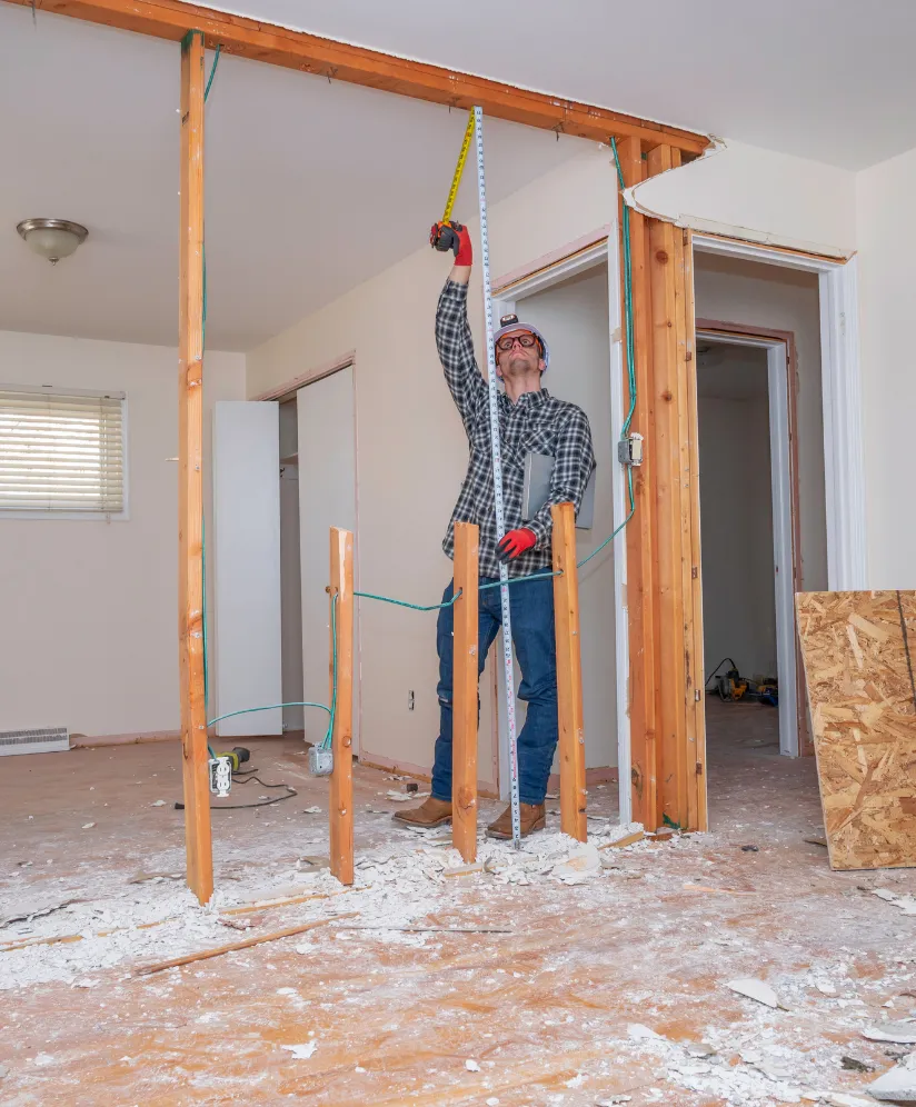 Los Angeles HOA remodeling services showing interior wall demolition, exposed wood framing, electrical wiring, contractor measuring the opening, and renovation preparation