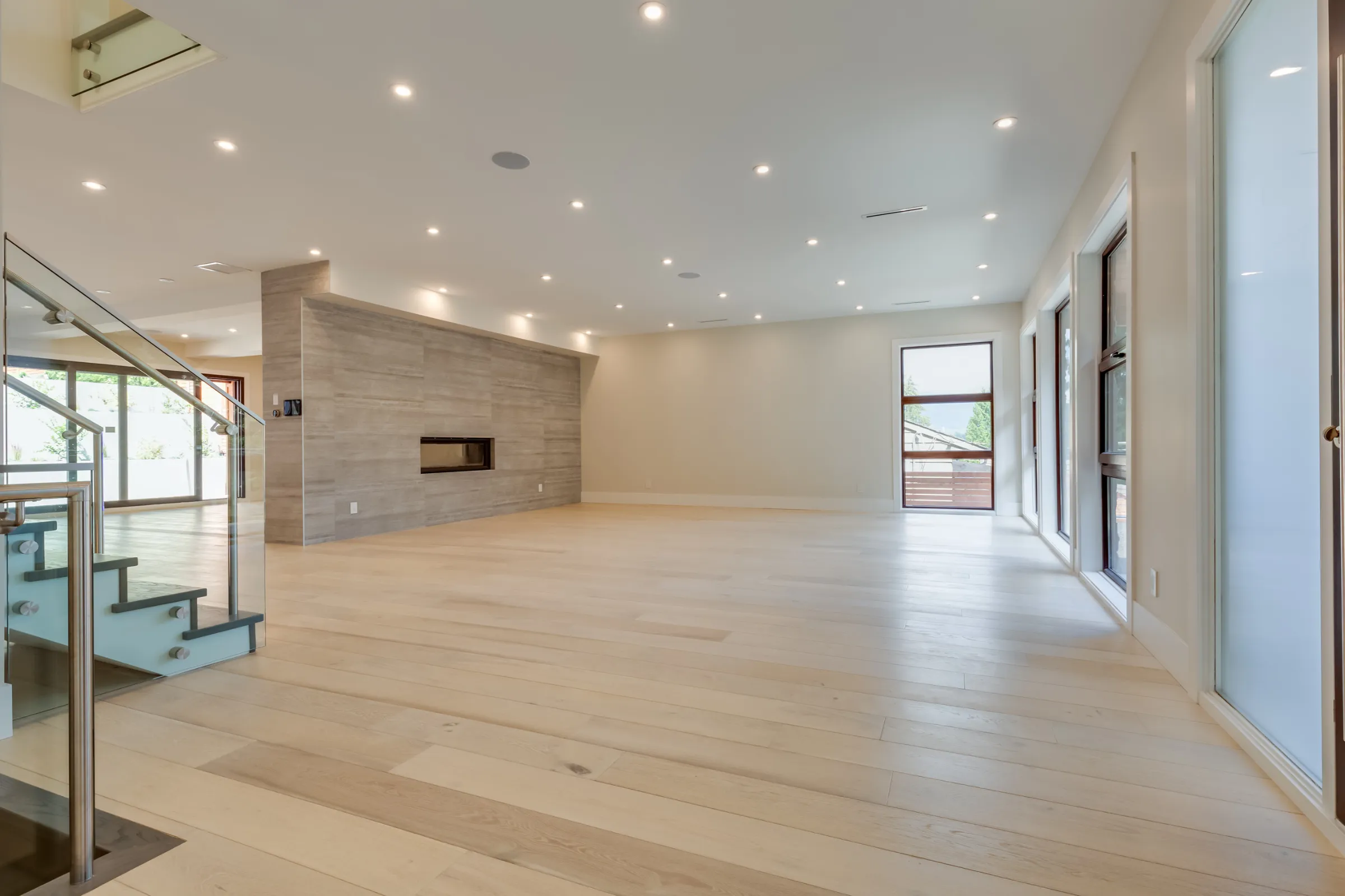 HOA remodeling services in Los Angeles showing a renovated common area with light wood flooring, recessed lighting, glass stair railing, large windows, and modern fireplace wall