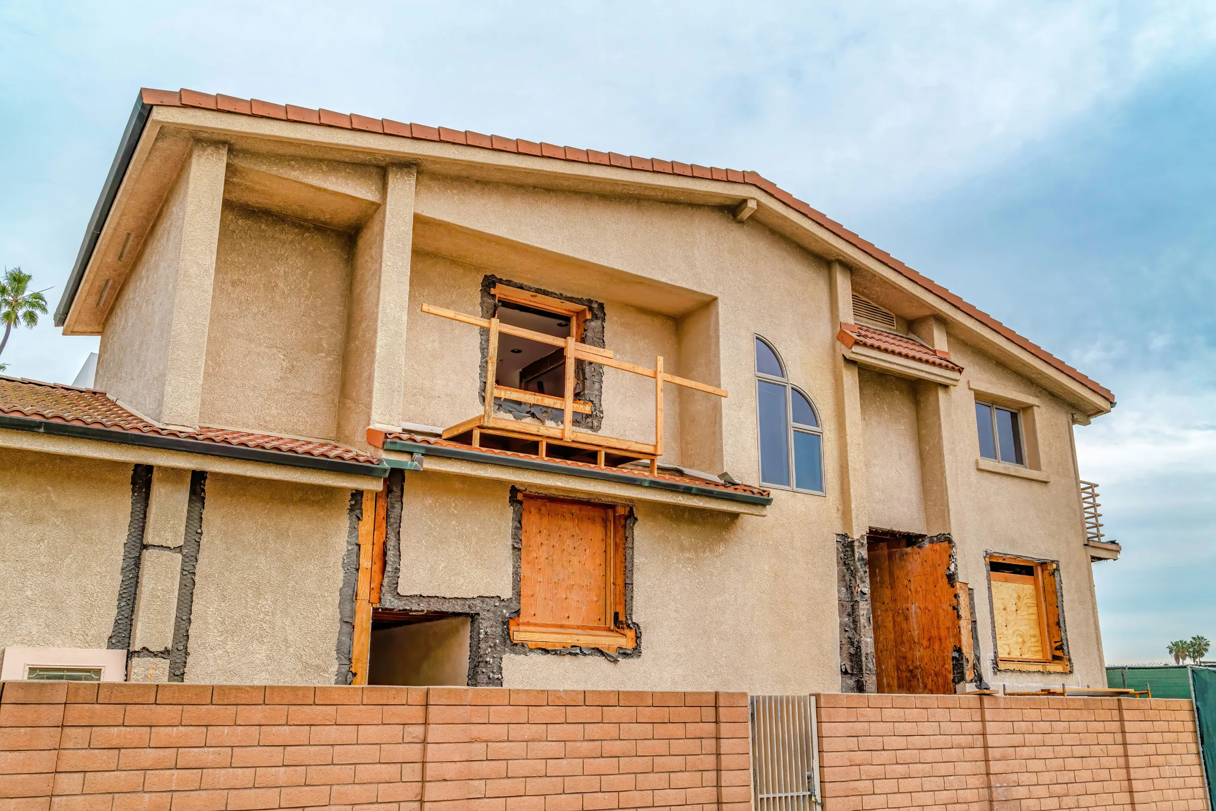 Residential remodeling in Los Angeles showing a two-story home exterior under renovation with stucco repair, boarded windows, wall openings, and construction preparation