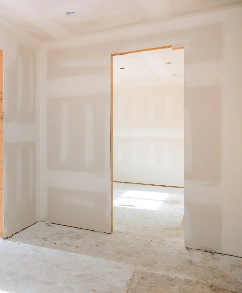 Los Angeles room addition project showing interior drywall installation, unfinished walls, open doorway, recessed ceiling lights, and construction flooring during build-out